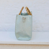 Light blue textured handbag with bamboo handles on a white surface.
