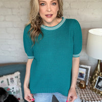 Woman wearing a teal sweater with white trim.