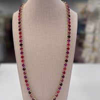Necklace with multicolored red, purple, pink stones on a beige bust against a blurred background