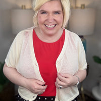 Woman wearing a cream cardigan and black polkadot print skirt indoors.