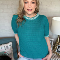 Woman wearing a teal sweater with white trim.
