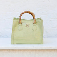 Light green handbag with wooden handle on a textured white surface