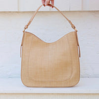 Beige handbag held by a hand against a light background