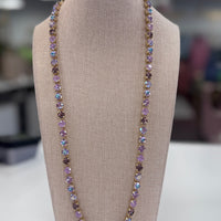 A purple necklace with iridescent stones displayed on a mannequin bust, set against a blurred indoor background.