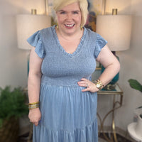 A woman wearing a light blue denim maxi dress with a smocked bodice and short ruffled sleeves