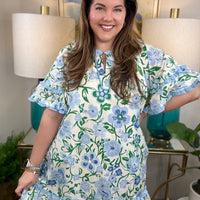 Woman wearing a blue and white ruffled dress with greenery accents.