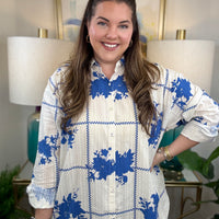 Woman wearing a white button down blouse with royal blue floral accents.