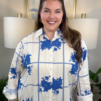 Woman wearing a white button down blouse with royal blue floral accents.