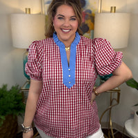 Woman wearing a red and white checkered blouse with blue trim in a room with lamps and artwork.