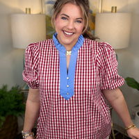 Woman wearing a red and white checkered shirt with blue trim in a room with lamps and a painting.