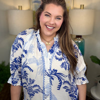 Woman wearing a white blouse with blue floral patterns in a room with lamps and a painting.