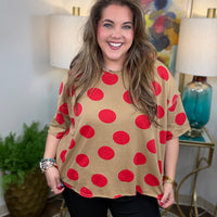 Woman wearing a beige shirt with red polka dots in a room with lamps and a painting.