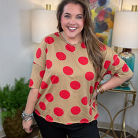 Woman wearing a beige shirt with red polka dots in a room with lamps and a painting.