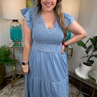 A woman wearing a light blue denim maxi dress with a smocked bodice and short ruffled sleeves