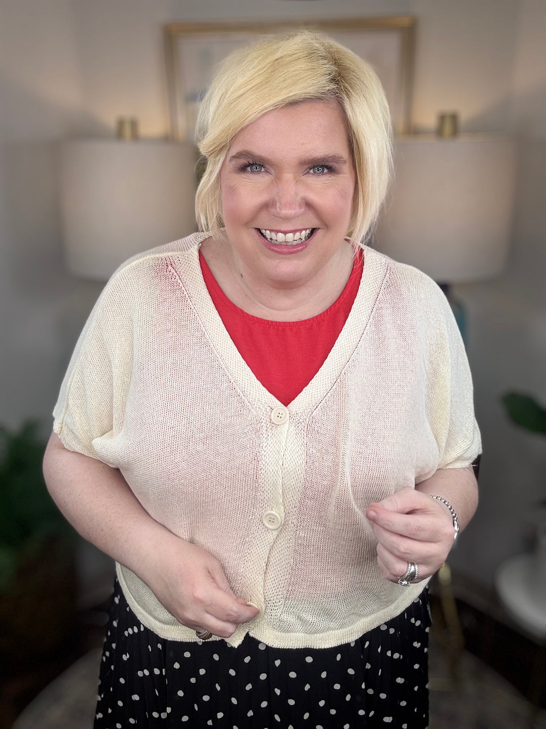 Woman wearing a cream cardigan and black polkadot print skirt indoors.