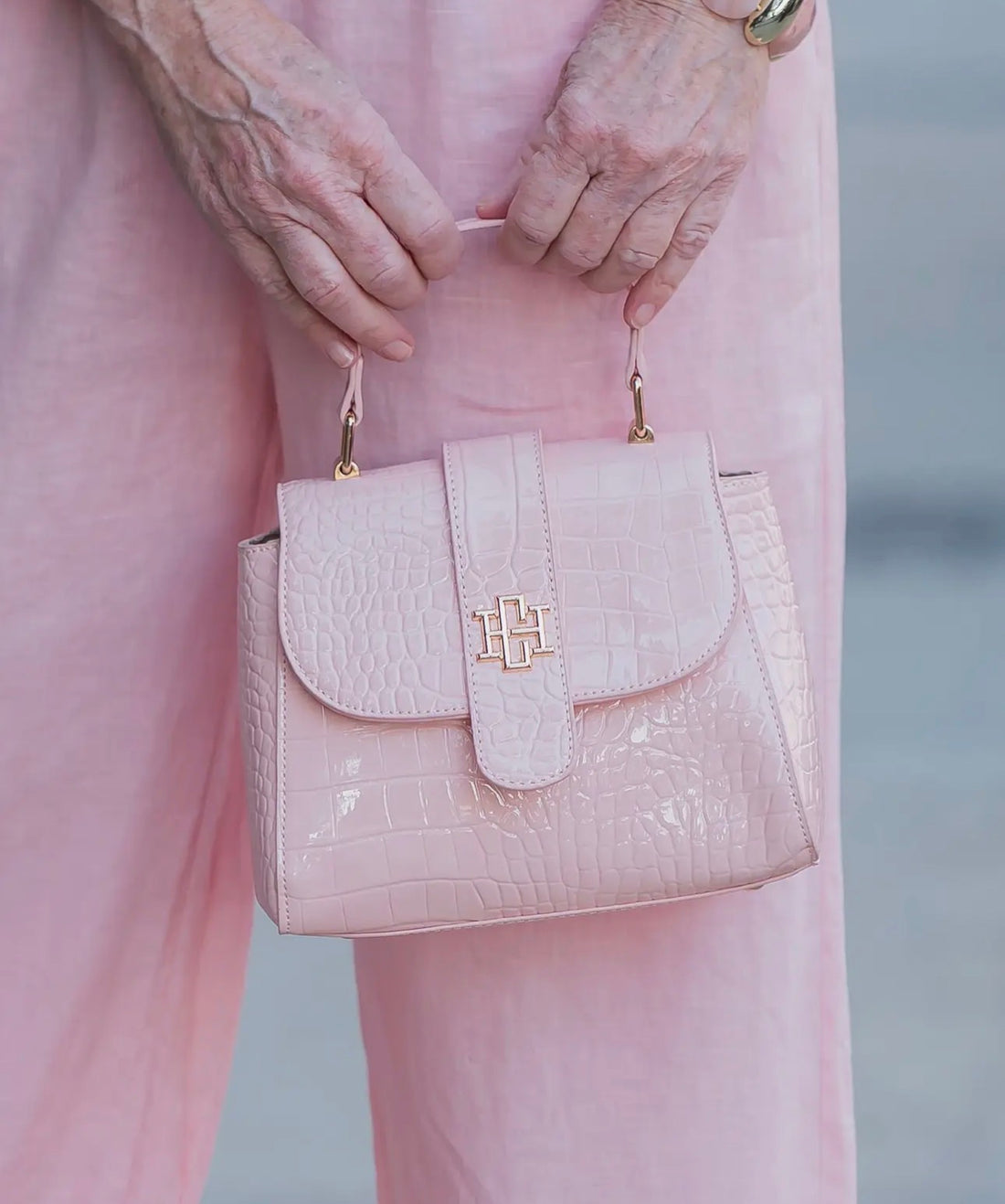 Pink handbag with gold accents held by a person wearing pink pants.