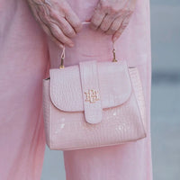 Pink handbag with gold accents held by a person wearing pink pants.