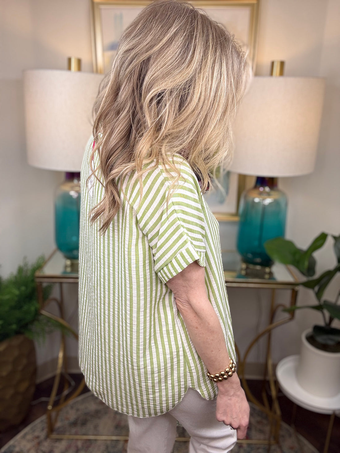 Person wearing a green and white striped shirt in a room with lamps and plants.