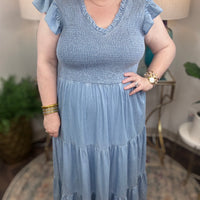 A woman wearing a light blue denim maxi dress with a smocked bodice and short ruffled sleeves