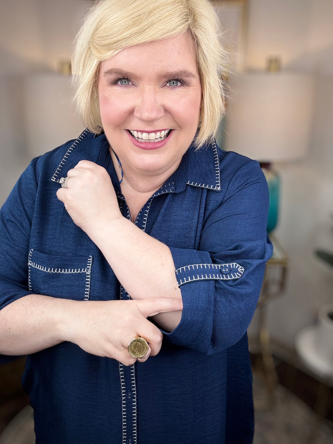 Woman wearing a navy shirt dress in a home setting with lamps and decor.