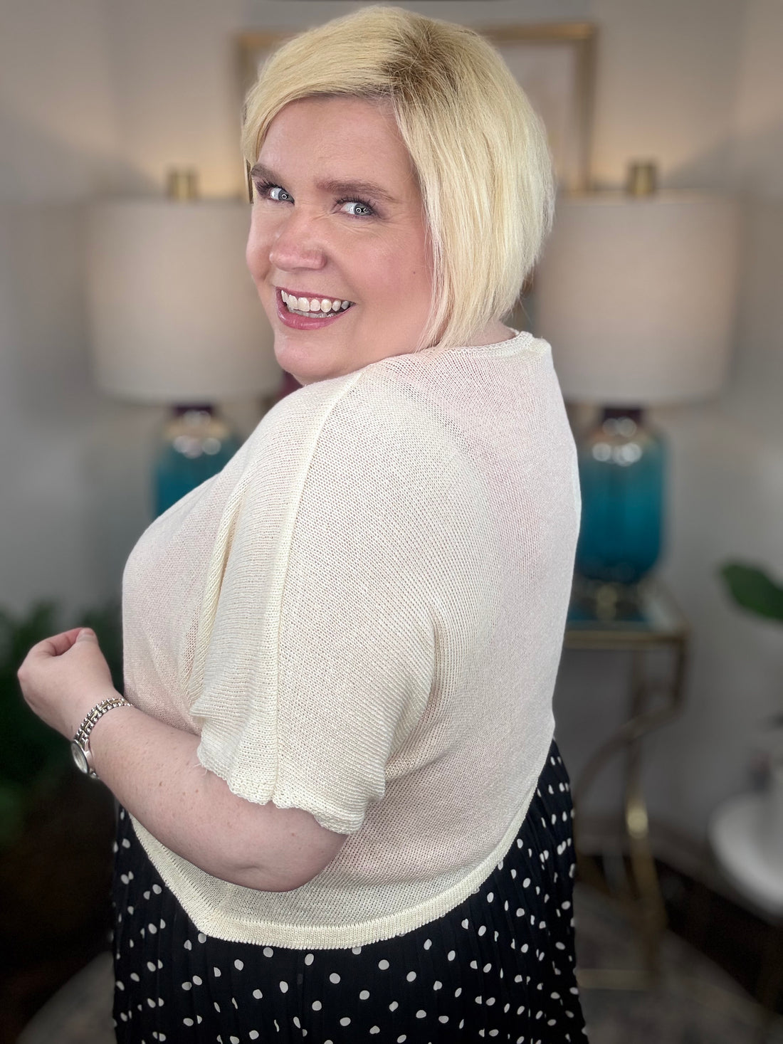 Woman wearing a cream cardigan and polkadot print skirt indoors.