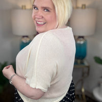 Woman wearing a cream cardigan and polkadot print skirt indoors.
