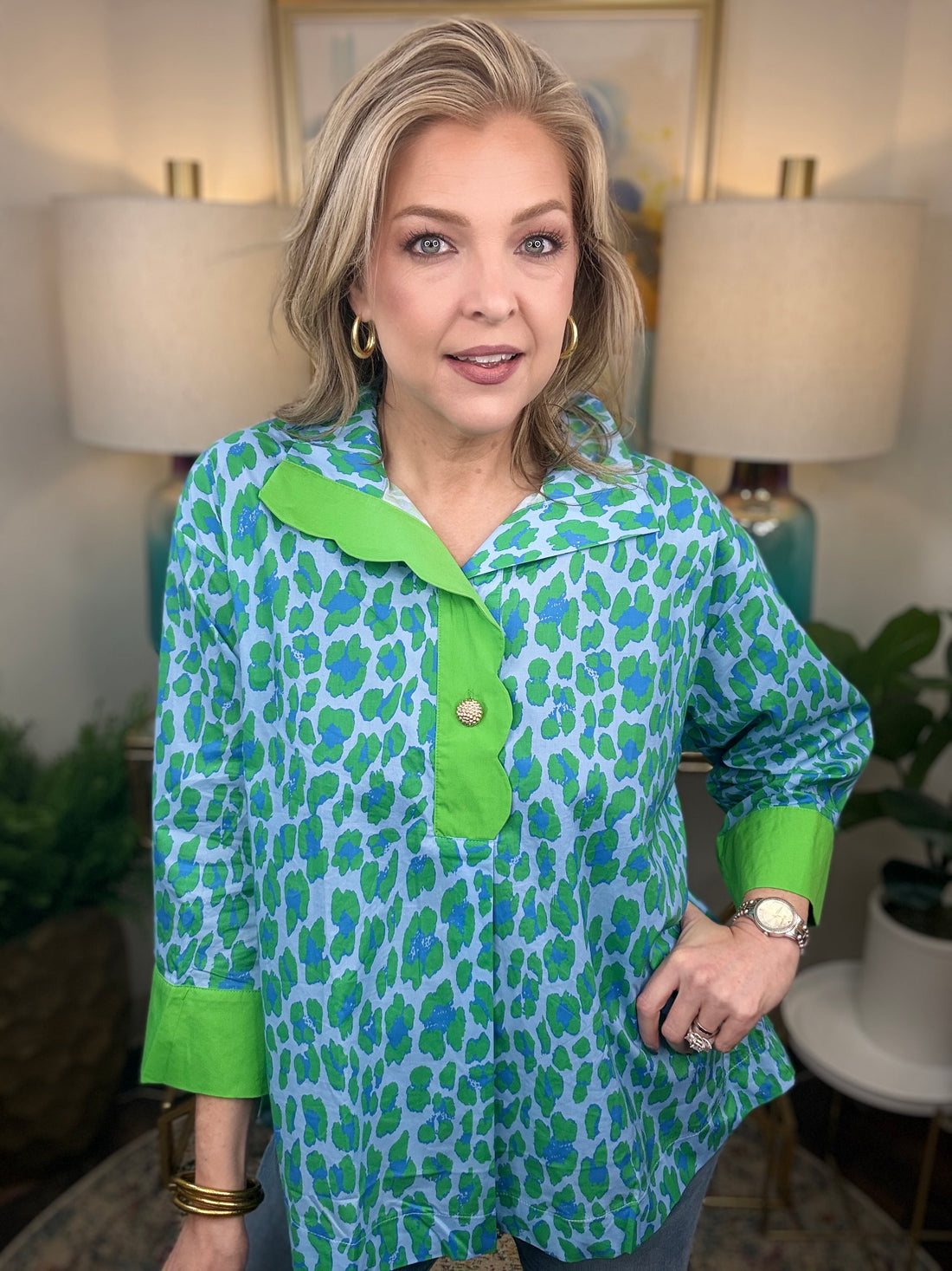 Woman wearing a green and blue patterned shirt in a home setting with lamps and artwork.