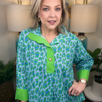 Woman wearing a green and blue patterned shirt in a home setting with lamps and artwork.