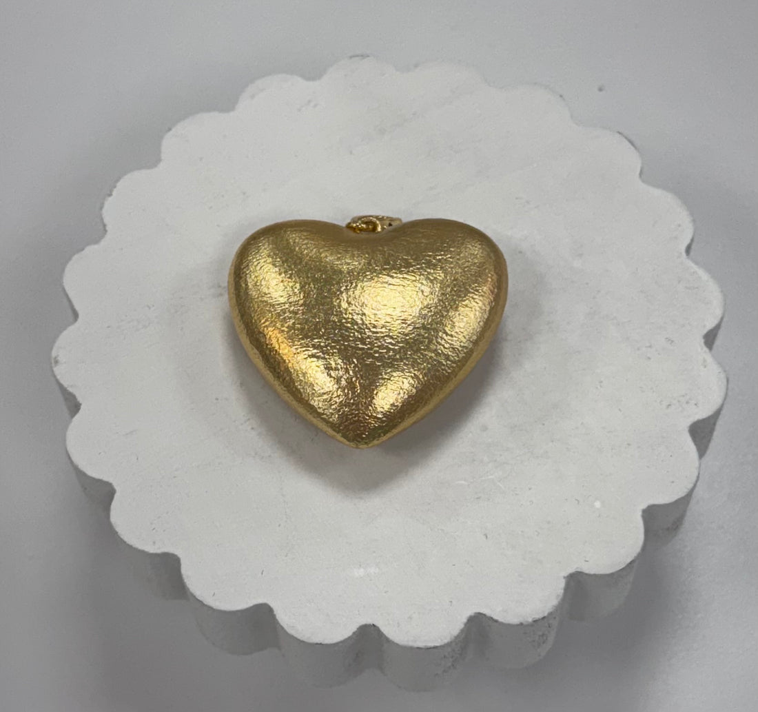 Gold heart-shaped pendant on a white scalloped edge stand.