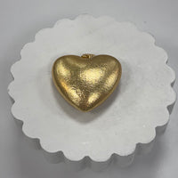 Gold heart-shaped pendant on a white scalloped edge stand.