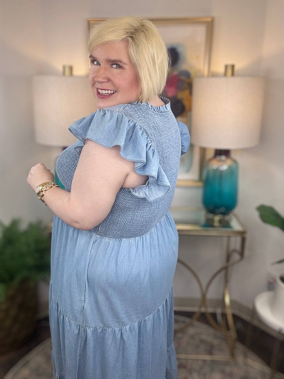 A woman wearing a light blue denim maxi dress with a smocked bodice and short ruffled sleeves