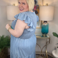 A woman wearing a light blue denim maxi dress with a smocked bodice and short ruffled sleeves