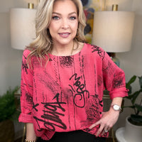 Woman wearing a pink top with black text in an indoor setting