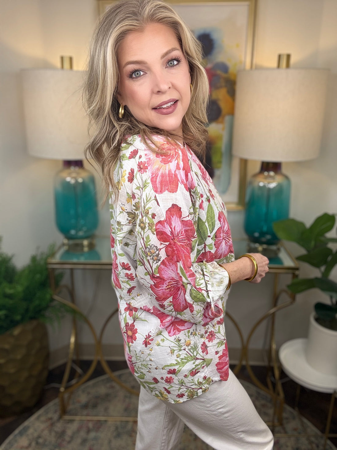 Woman wearing a floral blouse in a home setting with lamps and decor.