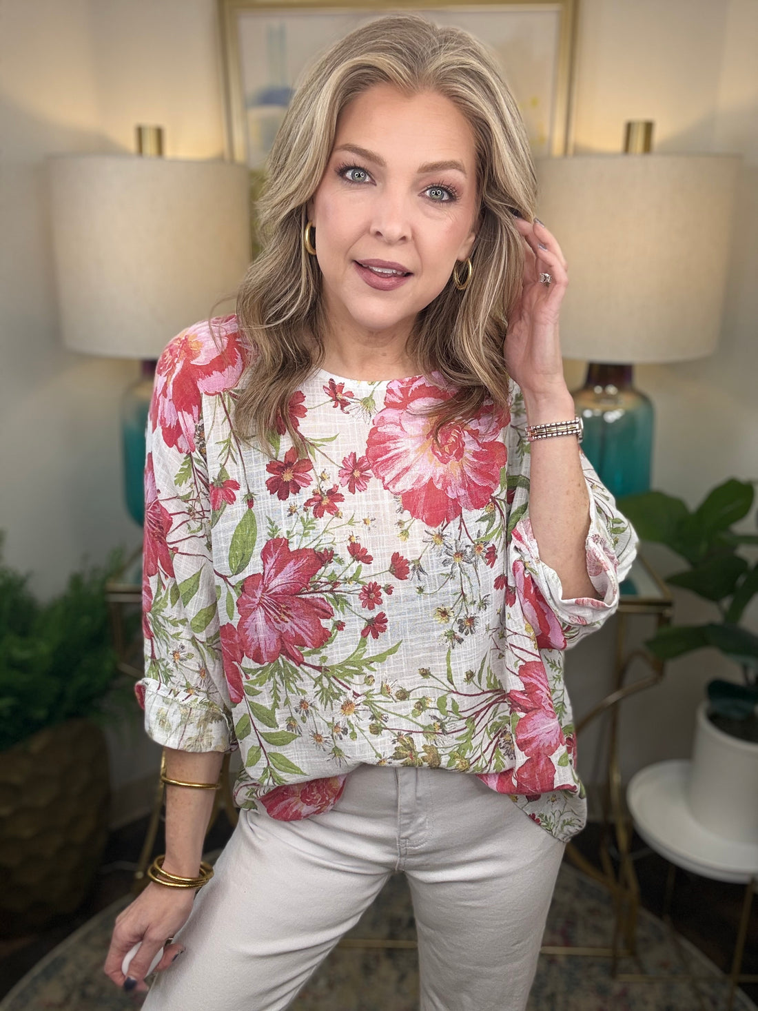 Woman wearing a floral blouse in a home setting with lamps and plants.