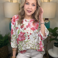 Woman wearing a floral blouse in a home setting with lamps and plants.