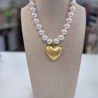 Pearl necklace with a gold heart pendant on a beige display stand.