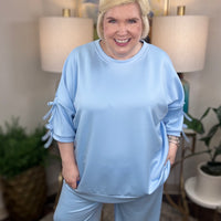 Woman wearing a baby blue matching set with bows tied on the sleeves.