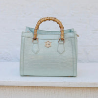 Light blue handbag with bamboo handle on a textured white surface