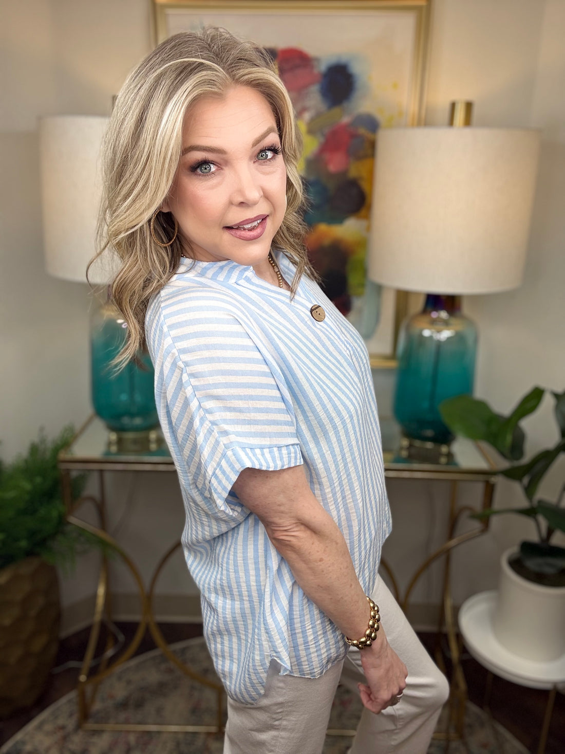 Woman in a striped shirt standing in a stylishly decorated room with lamps and artwork.