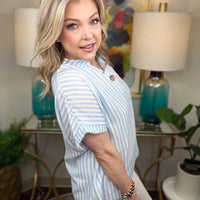 Woman in a striped shirt standing in a stylishly decorated room with lamps and artwork.