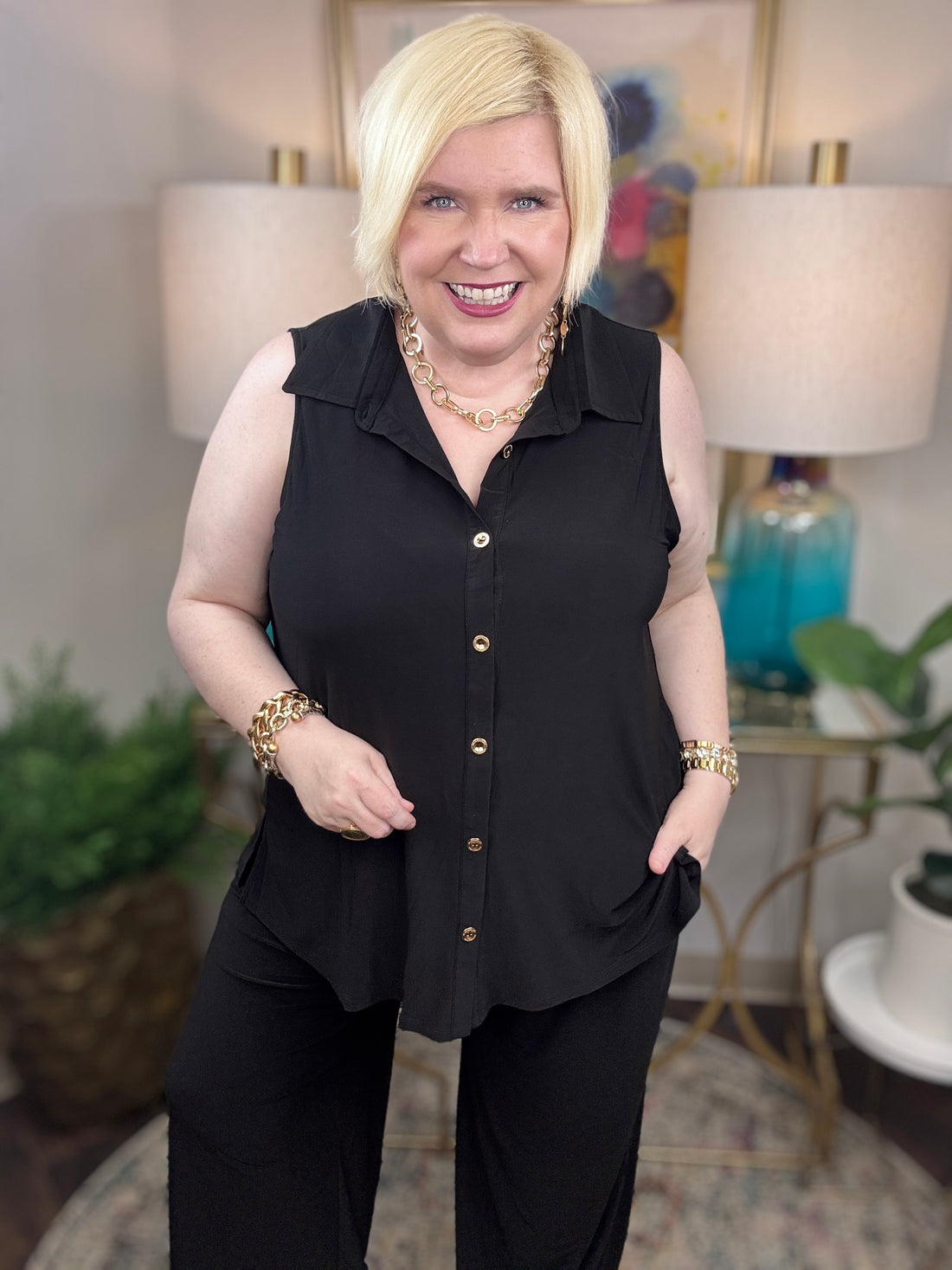 Woman wearing a black sleeveless top and pants with gold buttons.