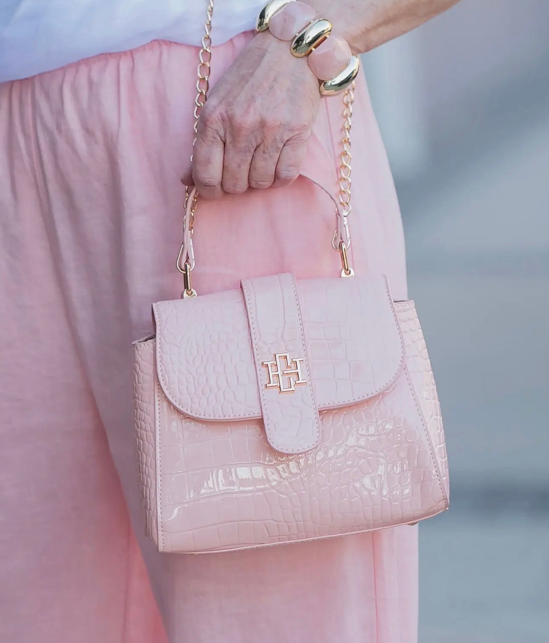 Pink handbag with gold chain held by a person wearing pink pants.