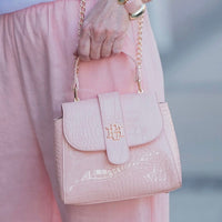 Pink handbag with gold chain held by a person wearing pink pants.