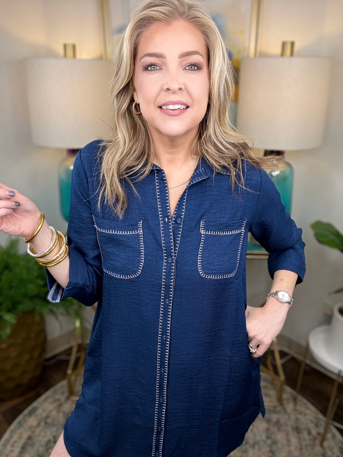 Woman wearing a navy shirt dress in a home setting with lamps and decor.