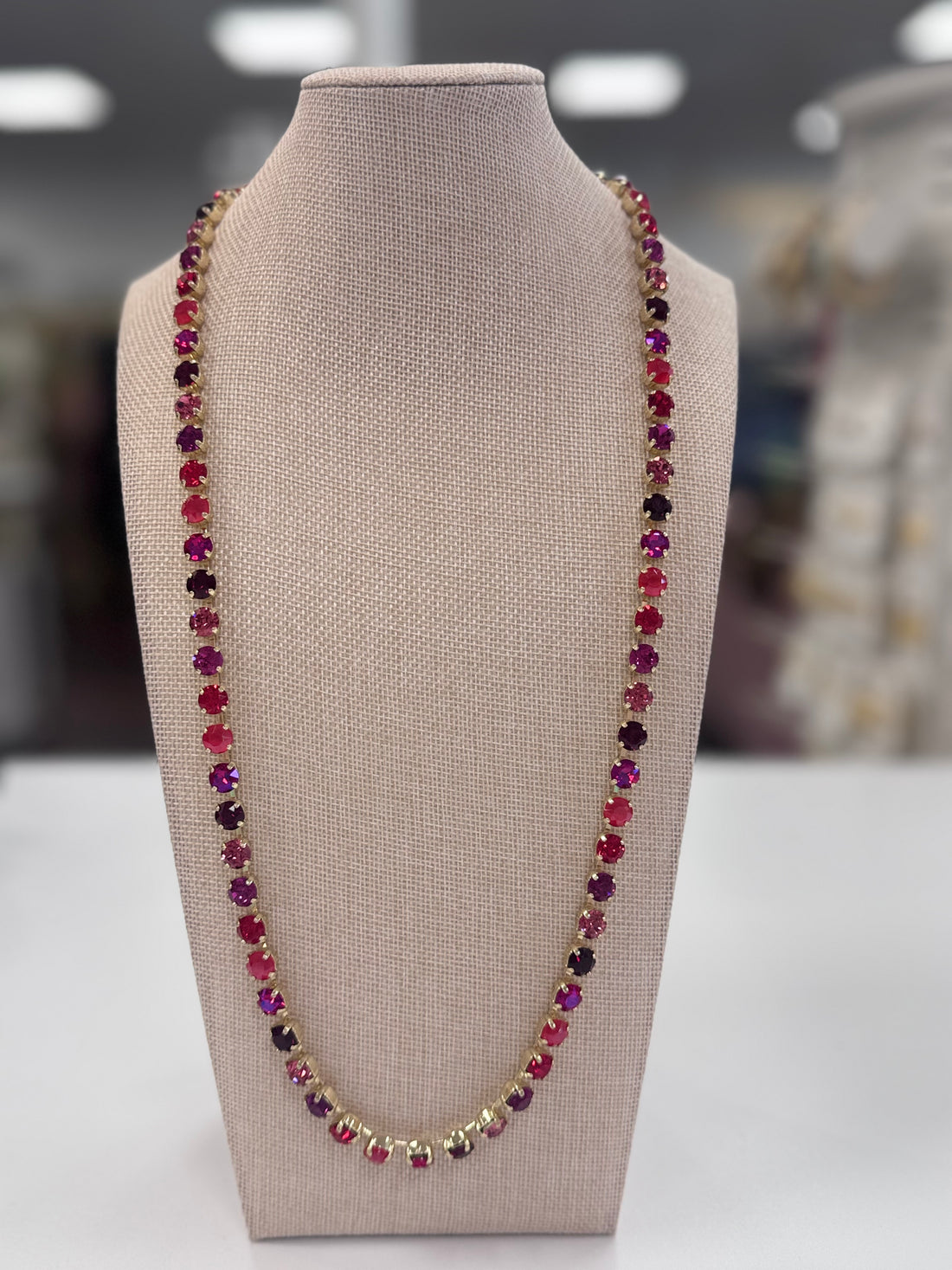 Necklace with multicolored red, purple, pink stones on a beige bust against a blurred background