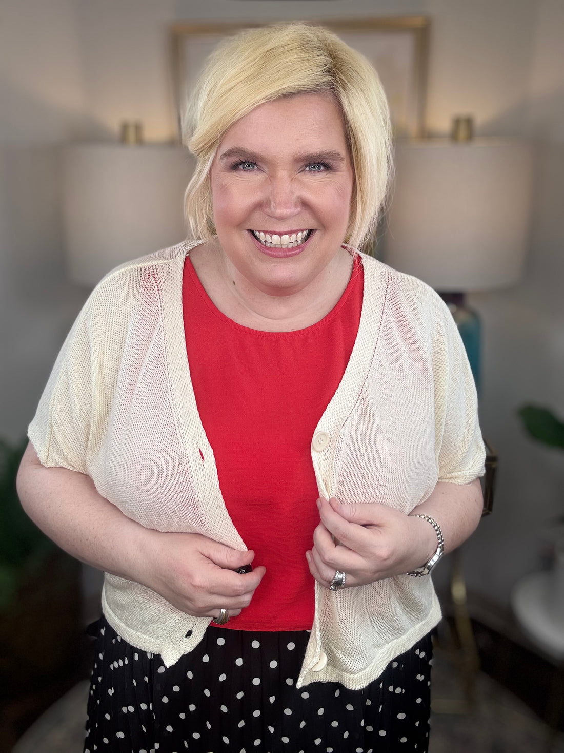 Woman wearing a cream cardigan and black polkadot print skirt indoors.