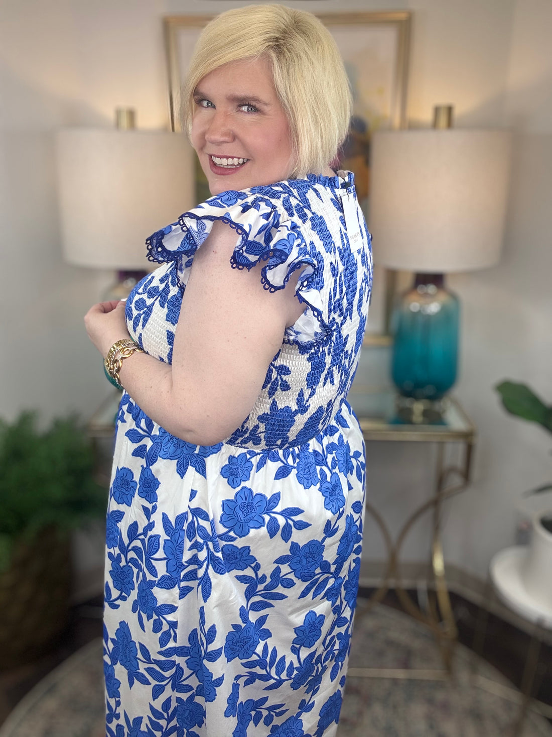 A woman with blonde hair wearing a white and blue floral print maxi dress with smocked bodice and ruffled cap sleeve