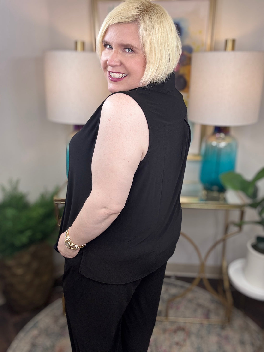 Woman wearing a black sleeveless top and pants with gold buttons