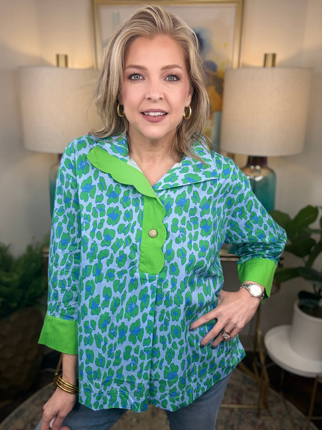 Woman wearing a green and blue patterned shirt in a home setting with lamps and artwork.